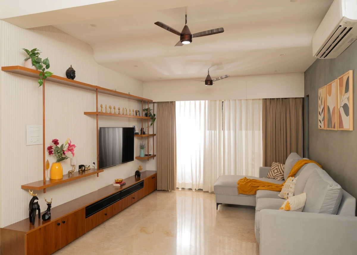 Warm daylight across a living room with a grey sofa, timber shelving and yellow cushions