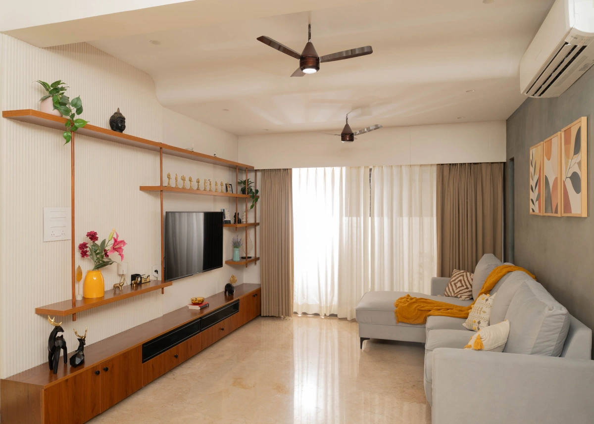 Warm daylight across a living room with a grey sofa, timber shelving and yellow cushions